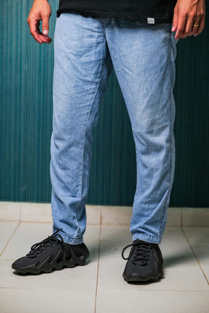 Close-up of a man wearing black sneakers and blue jeans indoors.