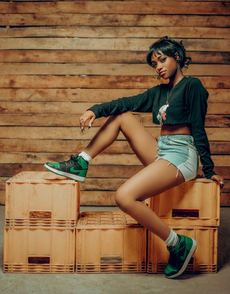 A fashionable young woman poses confidently against a wooden backdrop, showcasing modern casual style.