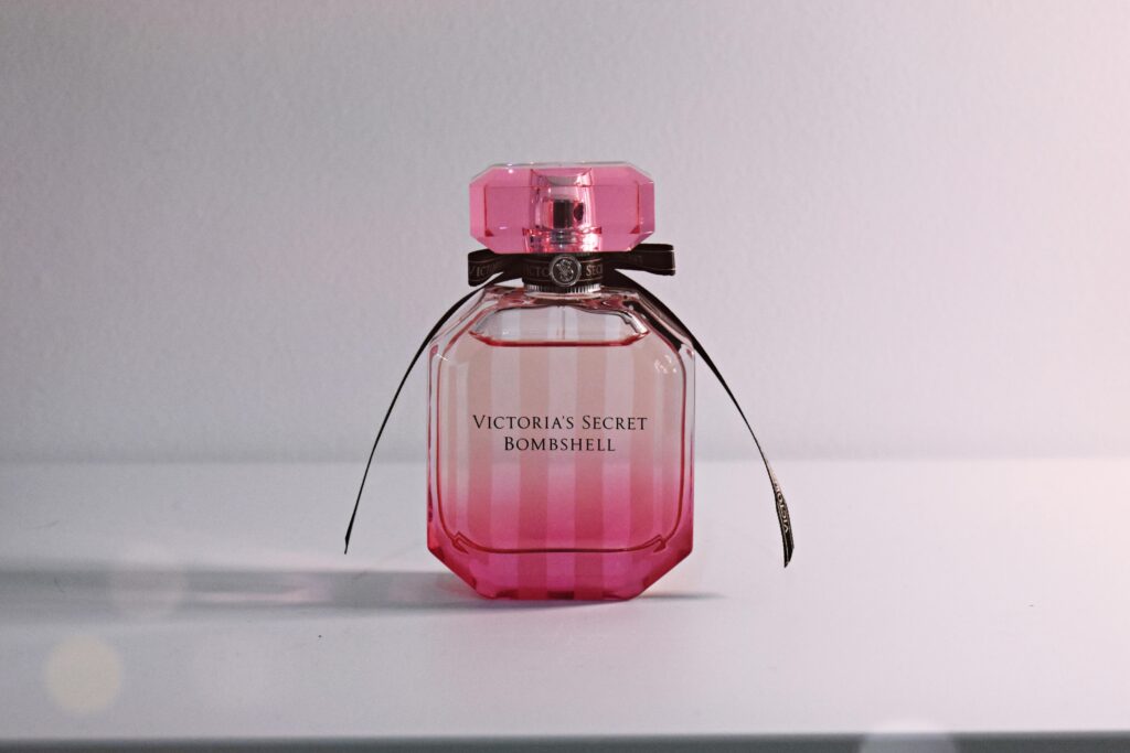 Stylish pink perfume bottle with bow and intricate cap on a white surface.